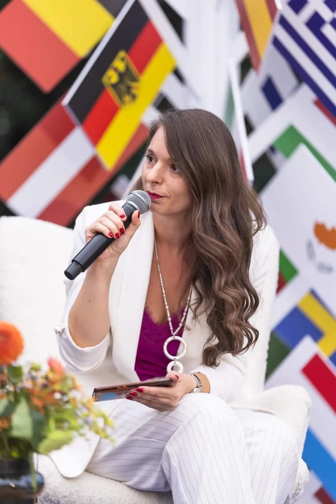 Alina Burlacu vorbind la microfon, în fața steagurilor participanților la un eveniment internațional